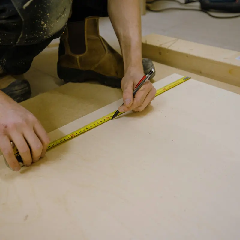 Hände messen mit Maßband und Bleistift auf einer Holzplatte